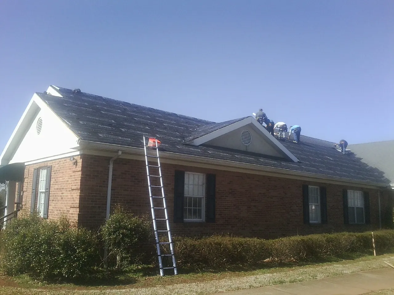 Crew tearing shingles off a brick ranch roof with a ladder set — Metal Roof Repair work by our crew in Hubbard