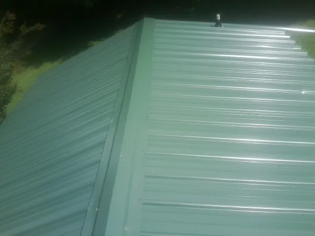 New green metal panels meeting at the ridge of a roof — Flat Roof Repair work by our crew in Hubbard